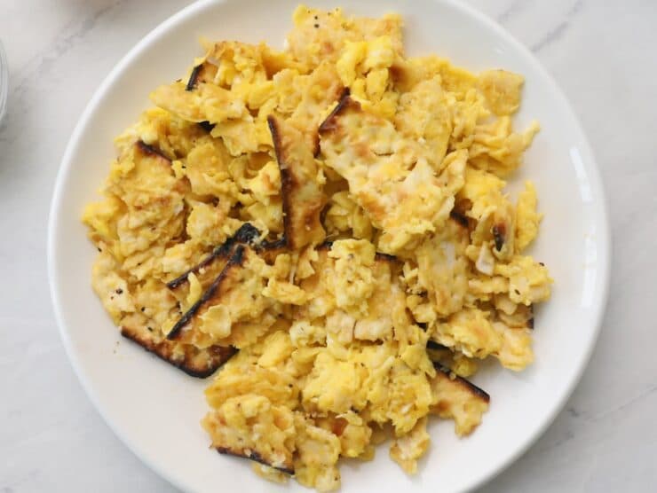 Horizontal closeup - a white plate with matzo brei eggs and matzo scrambled, on a white marble countertop.