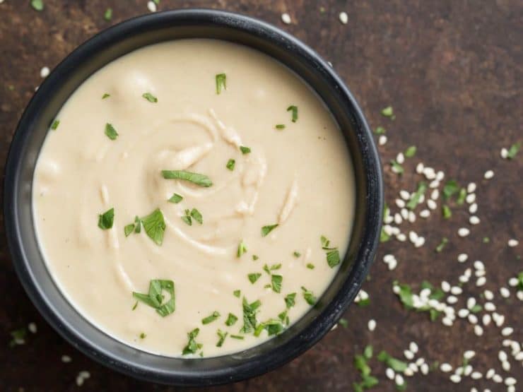 Bowl with tahini sauce with sesame seeds on countertop