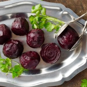 Roasted beets with parsley on silver tray with antique silver tongs.