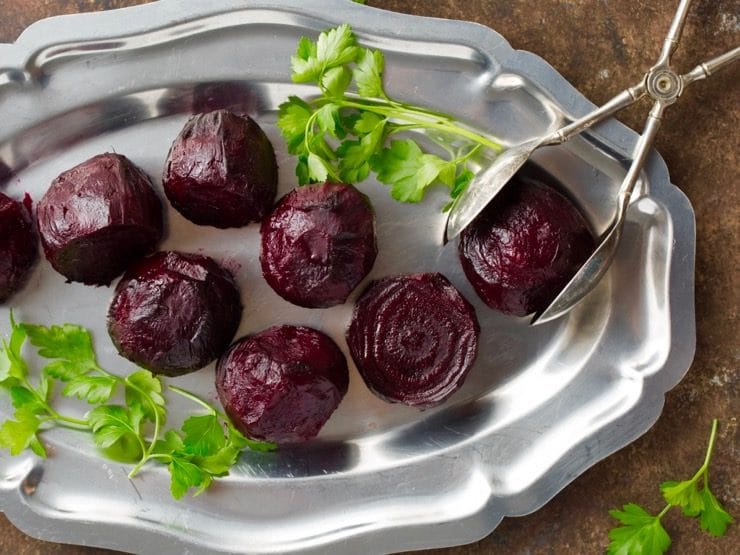 Roasted beets with parsley on silver tray with antique silver tongs.