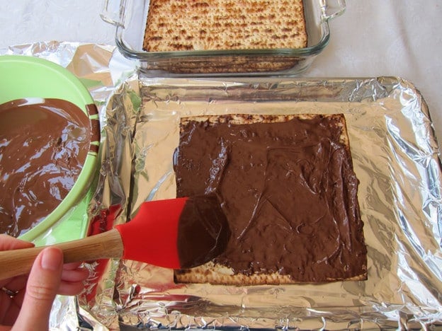 Spreading melted chocolate on matzo.