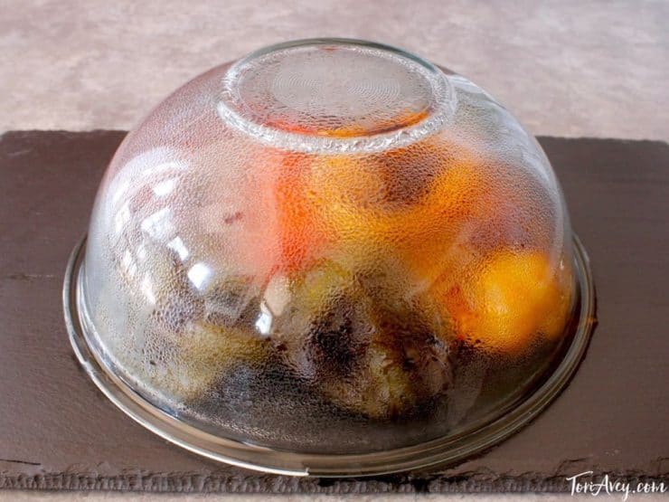 Roasted red bell peppers on cutting board steaming under glass bowl.