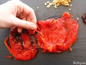 Roasted red bell pepper on cutting board, hand peeling skin.