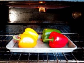 Colorful bell peppers on baking sheet under broiler.
