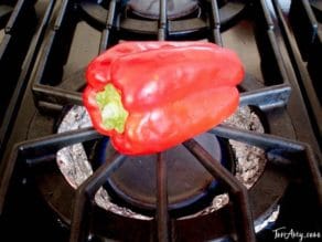 Red bell pepper roasting on gas stove.