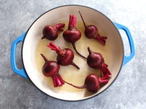 7 beets in a blue and white enamel cast iron casserole dish on a grey concrete background.
