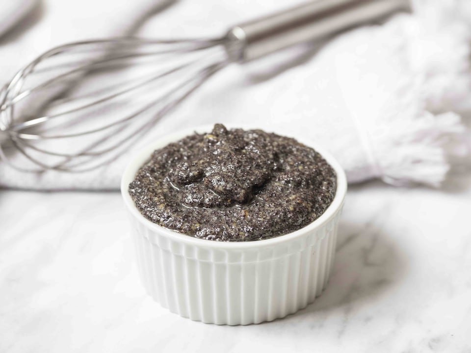 White ramekin of mohn - poppy seed filling on a marble background with whisk and towel behind. 