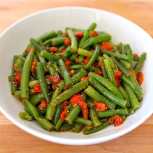 A vibrant mix of crisp green beans and colorful pepper on a white bowl