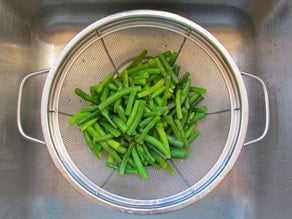 Draining blanched green beans in a strainer.
