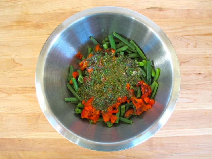 Dressing poured over green beans in a mixing bowl.
