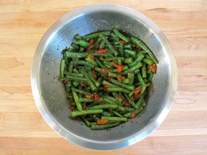 Green beans tossed with dressing in a bowl.