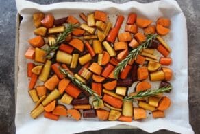Cut up root vegetables on parchment-lined baking sheet with rosemary sprigs.
