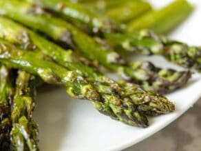 Close up of crisp roasted asparagus tips piled on a white plate.