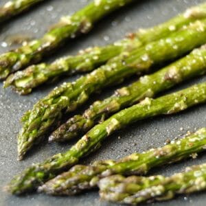 Close up of crisp roasted asparagus tips lined up on a baking sheet with salt.