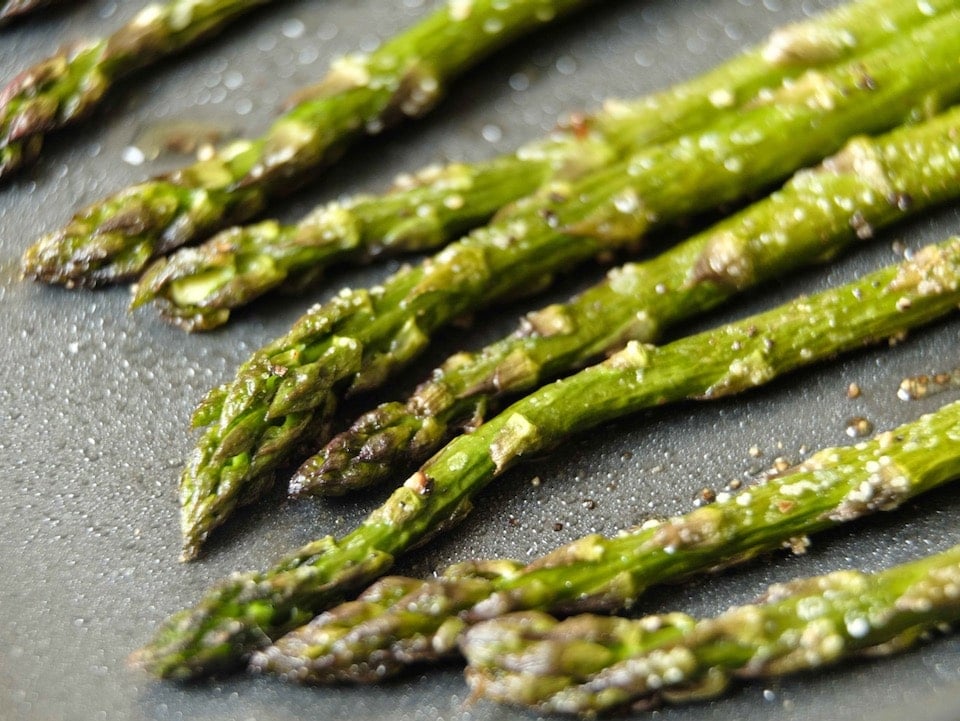 Close up of crisp roasted asparagus tips lined up on a baking sheet with salt.