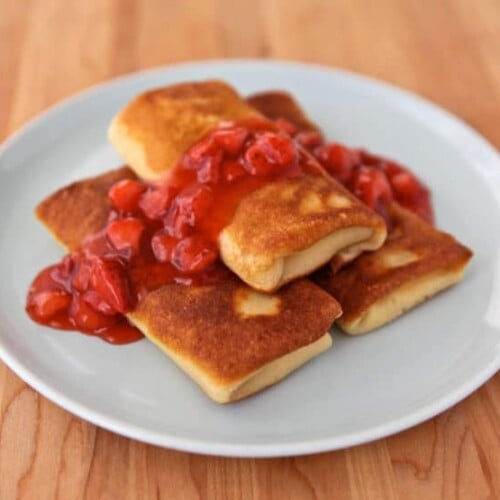 Three blintzes with strawberry topping sauce served on a white plate