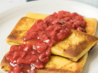 Cheese blintzes with strawberry sauce served on a white plate