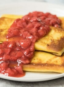 Close up horizontal shot - 3 cheese blintzes on a white plate, topped with strawberry topping