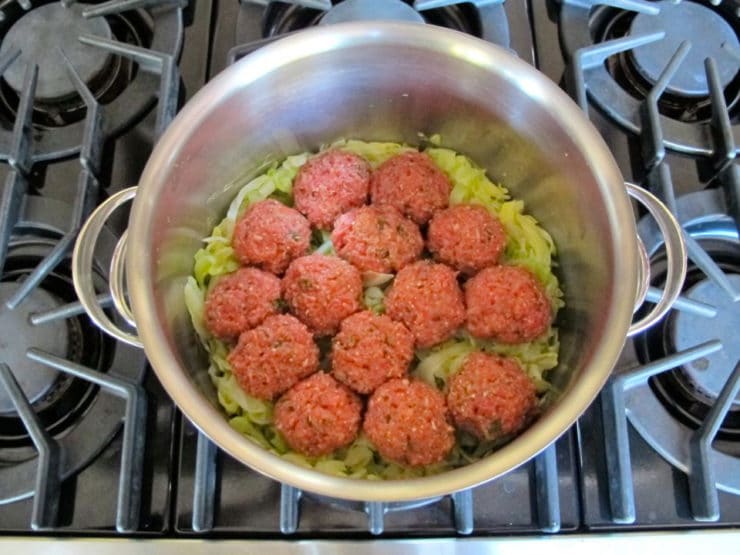 Meat mixture formed into balls and placed on steamed cabbage in a pot.