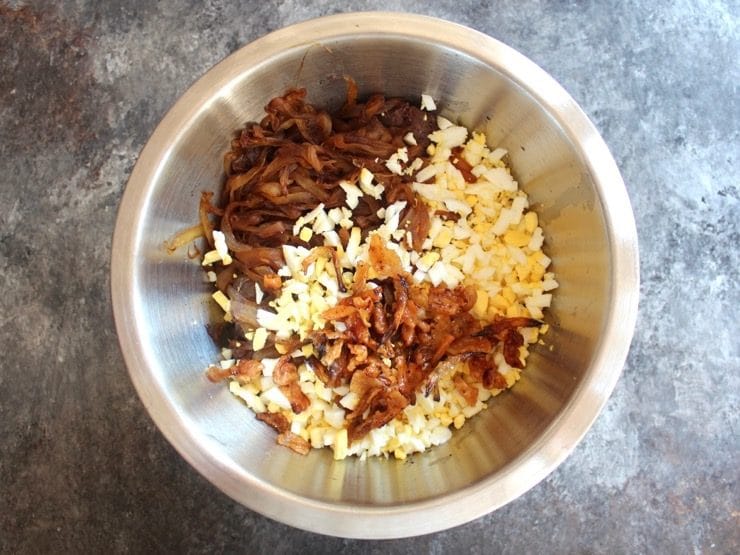 Stainless steel bowl filled with cooked chicken livers, diced hard boiled eggs, gribenes, caramelized onions.