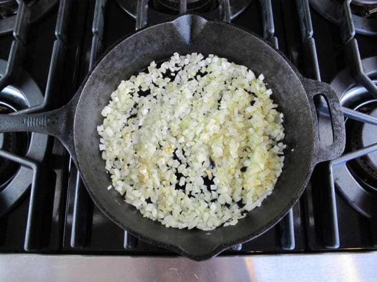Onion sautéing in black cast iron frying pan on stovetop.
