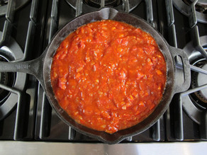 Diced tomatoes, pepper and onion sautéing in black cast iron frying pan on stovetop.