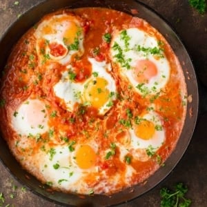 Eggs cooked in tomato sauce in a skillet topped with chopped herbs