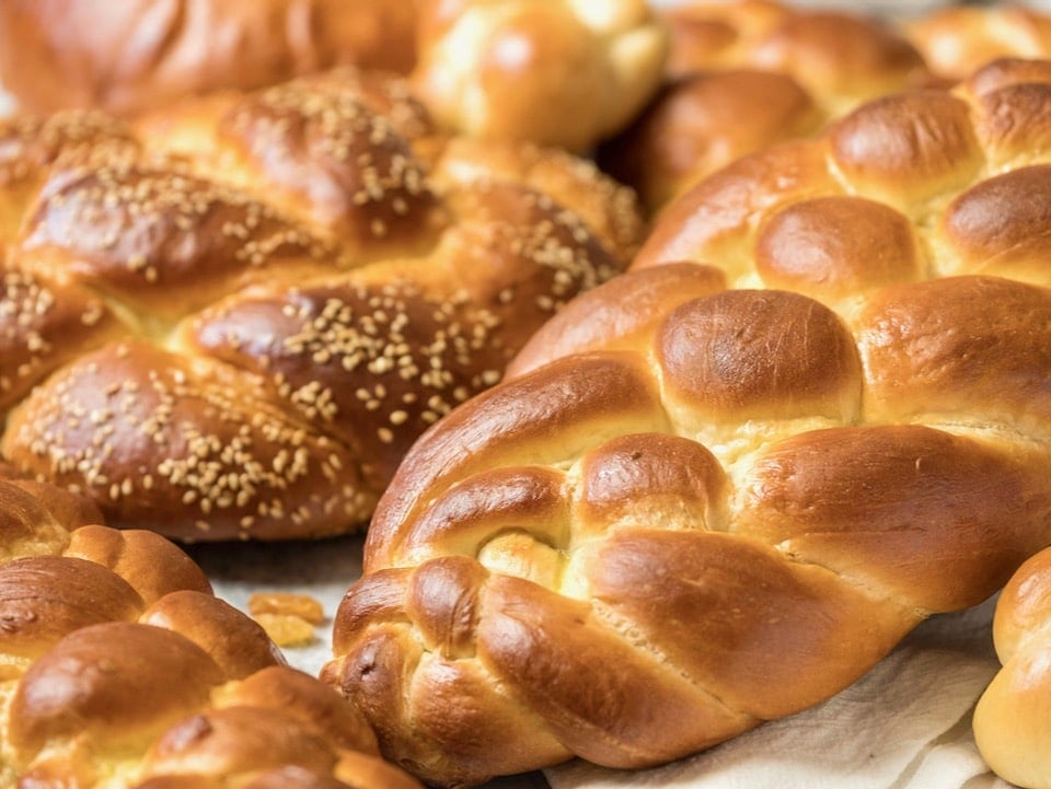 Several loaves of braided challah bread - multiple braiding styles - in a pretty pile on countertop.