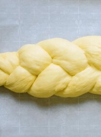 Square Crop Featured Image - Braided challah dough on parchment-lined baking sheet.