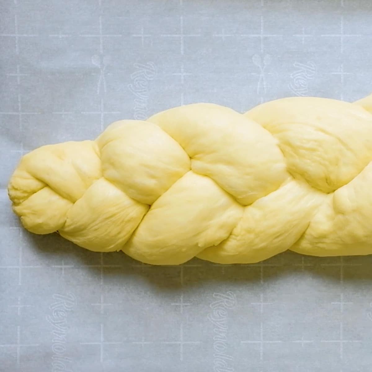 Square Crop Featured Image - Braided challah dough on parchment-lined baking sheet.