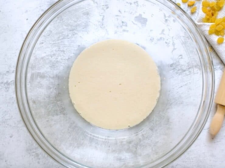 Yeast rising in glass mixing bowl on marble countertop.