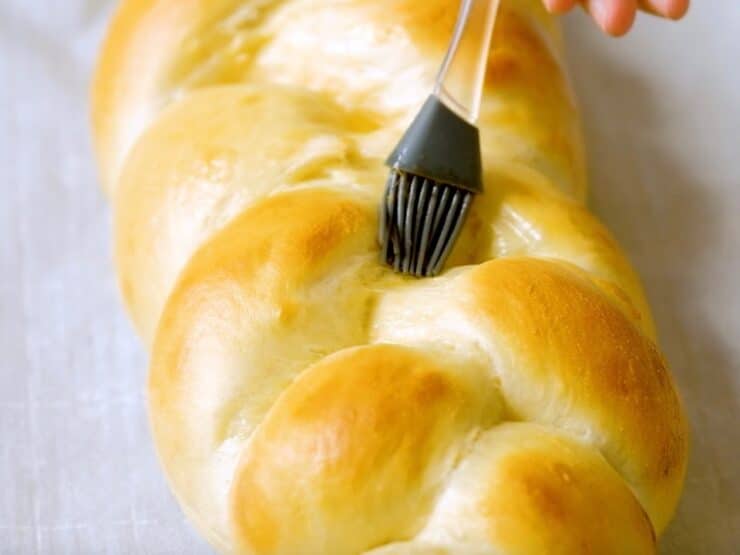 Silicone brush touching up the center of half-baked challah braid with egg wash.