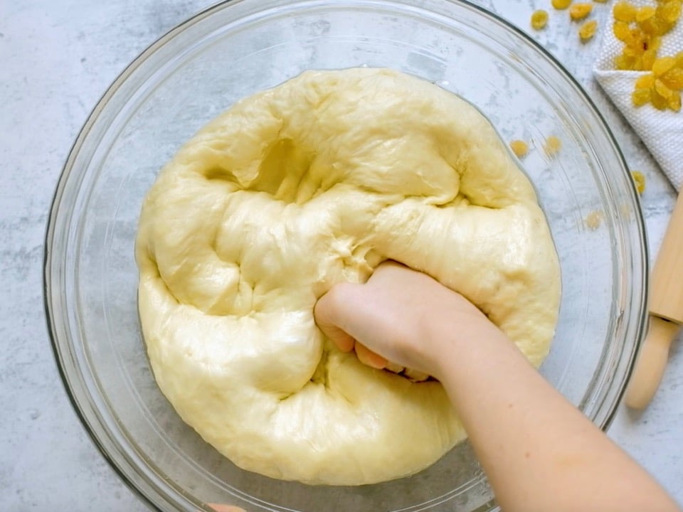 Hands kneading loose dough with flour in glass bowl on marble countertop.