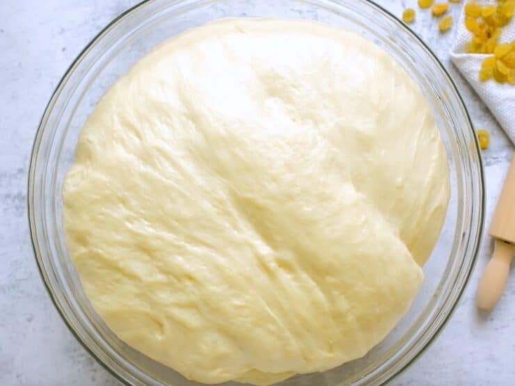 Risen puffy challah dough in glass bowl on marble countertop.