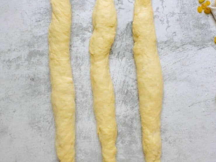 Overhead shot of three equal strands of challah laying next to each other.