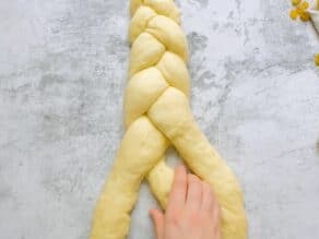Overhead shot of hands braiding challah dough into a three strand braid.