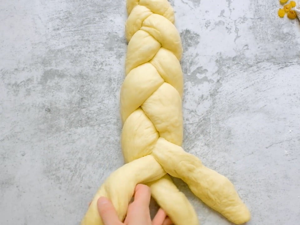 Overhead shot of two hands braiding the ends of a three strand challah dough braid.