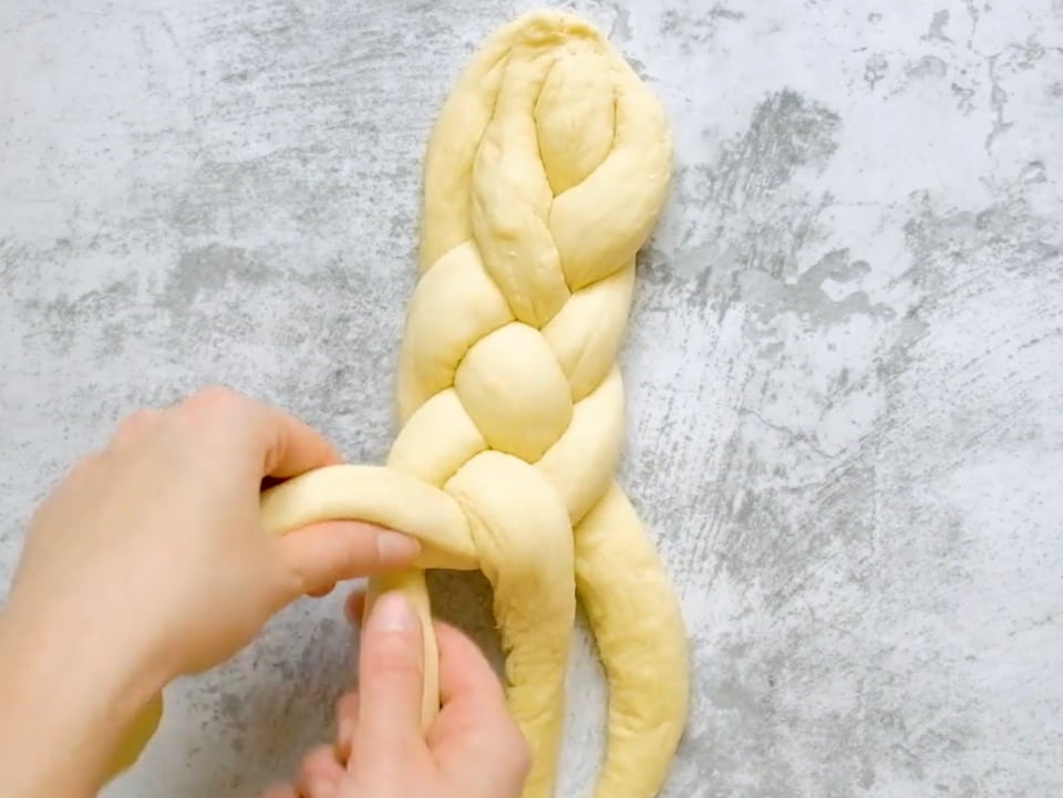 Overhead shot of two hands braiding a 4 strand challah.