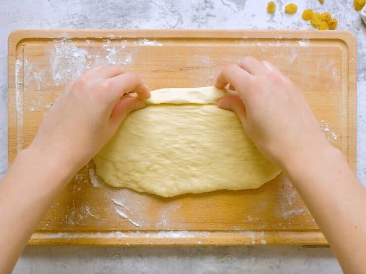 Overhead shot of two hands beginning to roll the challah dough into a strand.