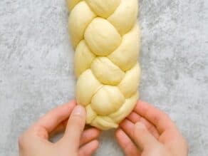 Overhead shot of two hands pinching together the ends of a four strand challah dough braid.