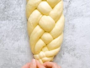 Overhead shot of two hands pinching together the ends of a six strand challah dough braid.