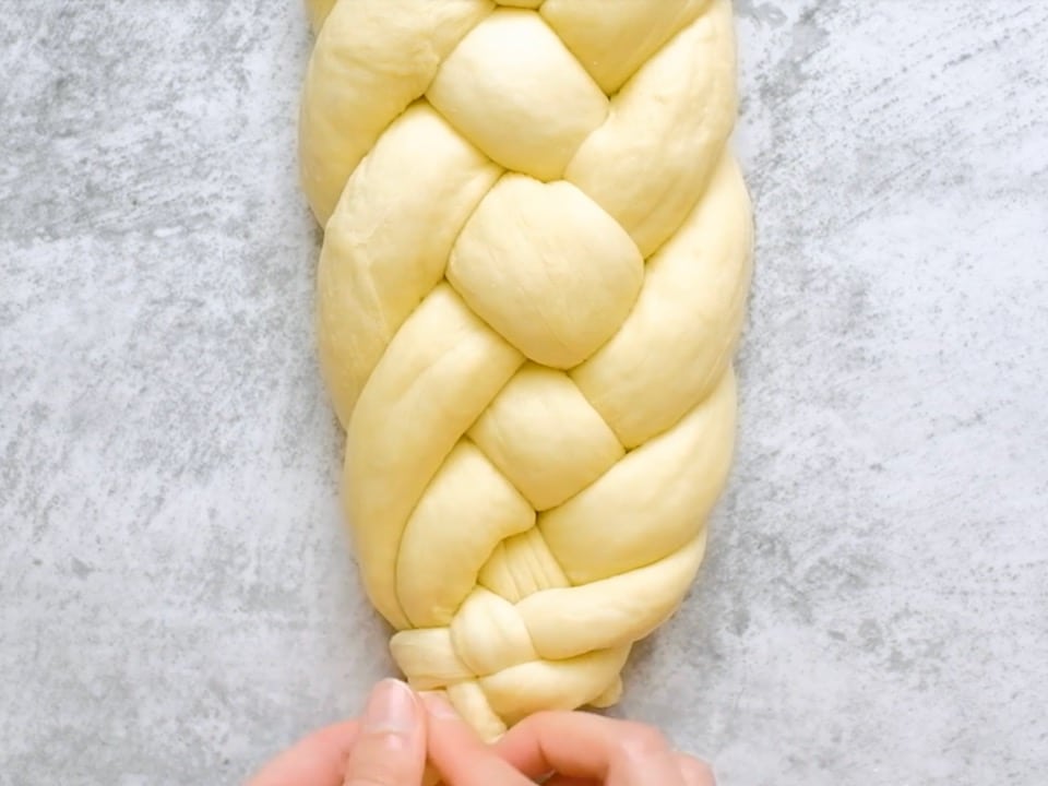 Overhead shot of two hands pinching together the ends of a six strand challah dough braid.