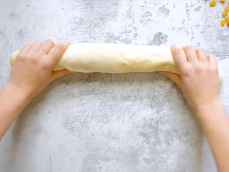 Overhead shot of two hands rolling challah dough into strand.