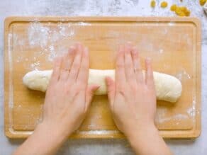Overhead shot of two hands rolling challah dough into a single strand.