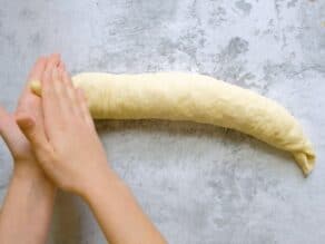Overhead shot of two hands rolling the end of the challah dough strand into a taper.