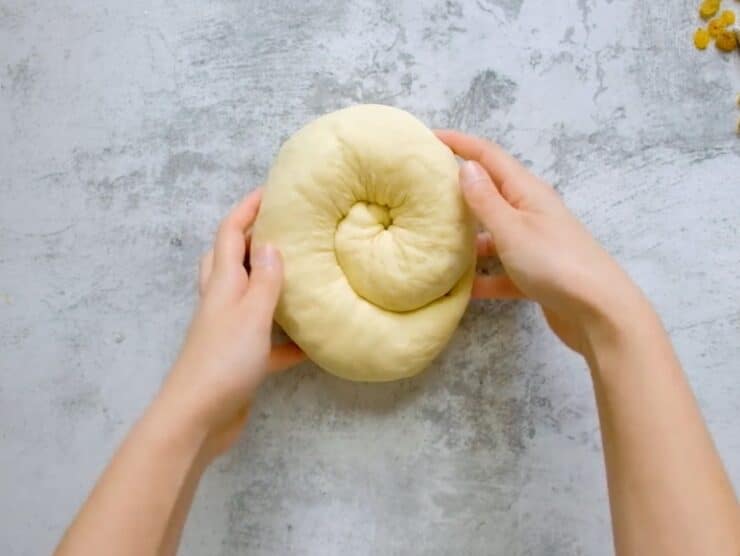 Overhead shot of two hands holding a coil of challah dough, known as a turban challah.