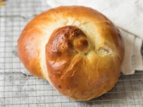Horizontal shot of fully baked snail-shaped turban challah, baked golden brown, on wire cooling rack with linen napkin.