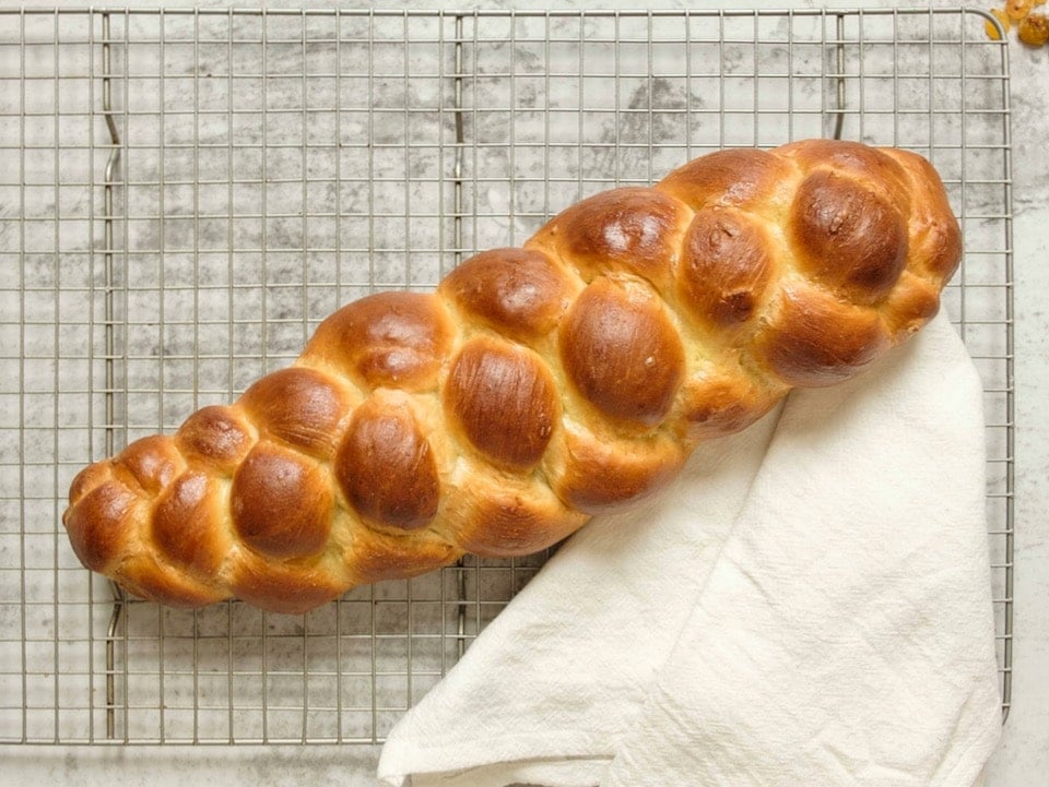 Overhead shot of fully baked 4 strand challah on cooling rack with linen cloth.