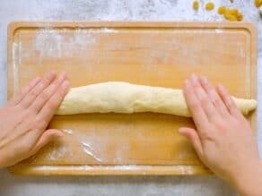 Overhead shot of two hands rolling challah dough into a single strand.