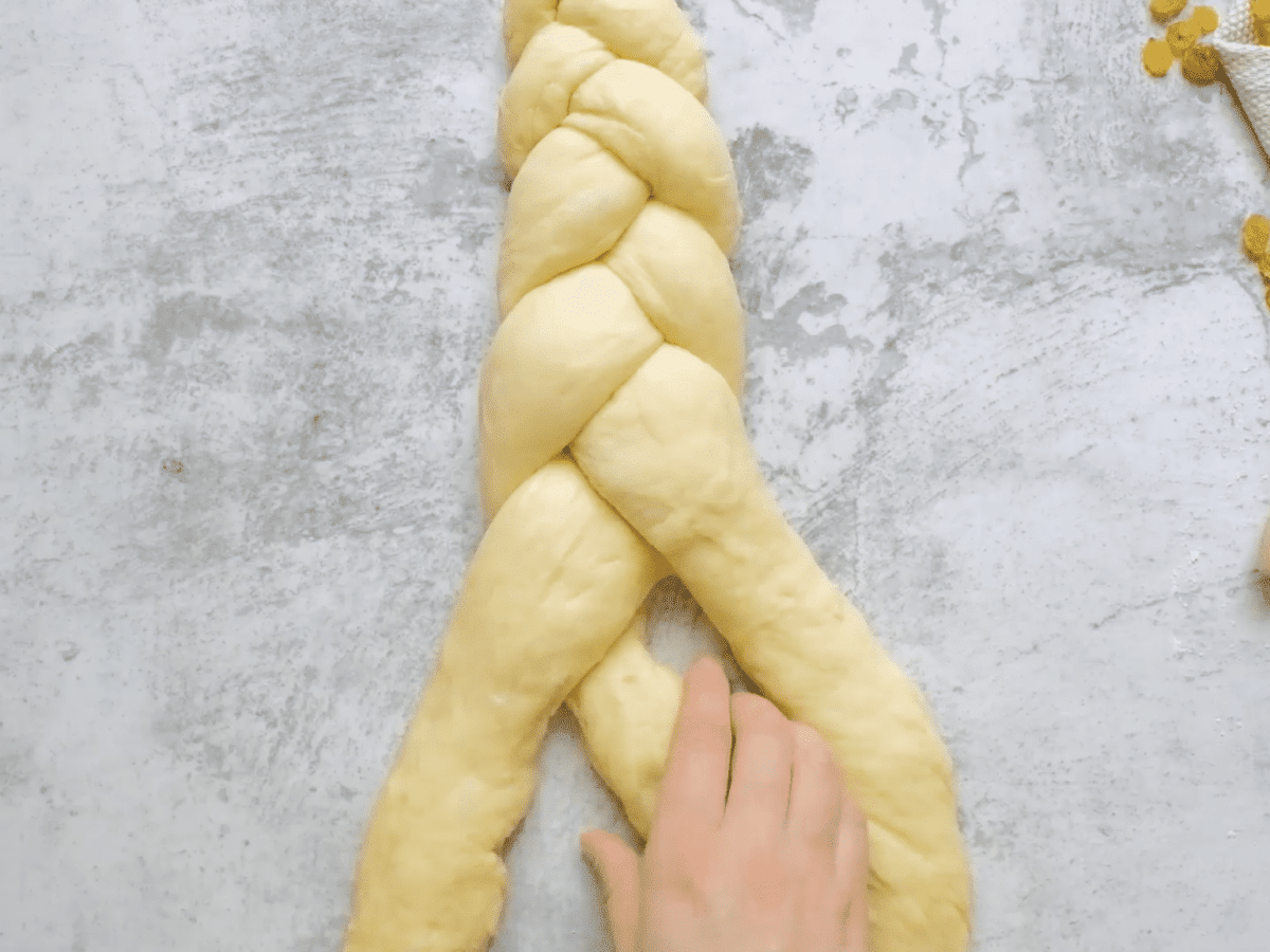 Overhead shot of hands braiding challah dough into a three strand braid.